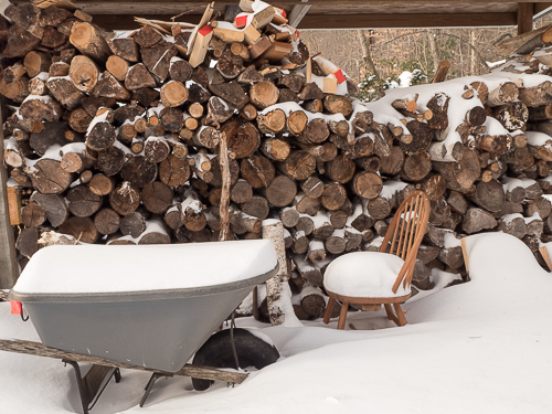 woodpile, wheelbarrow and chair full of snow